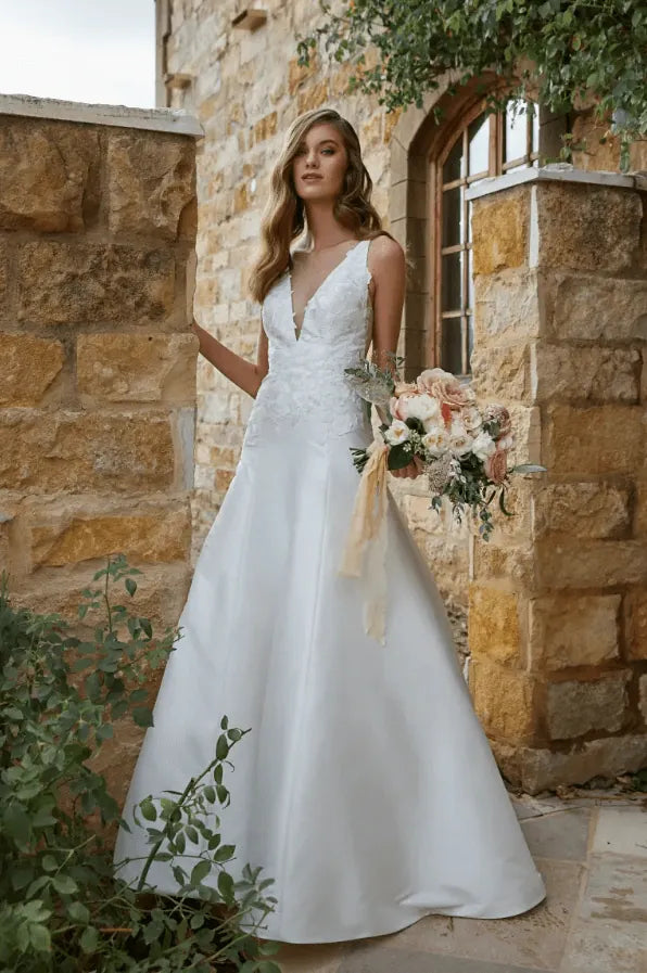 Woman in a white wedding dress holding flowers in front of a stone building.