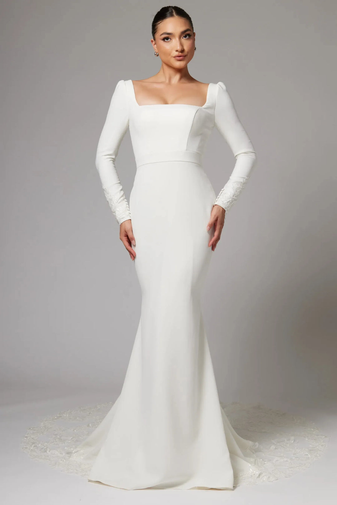 Woman wearing a white wedding dress with long sleeves on a plain background