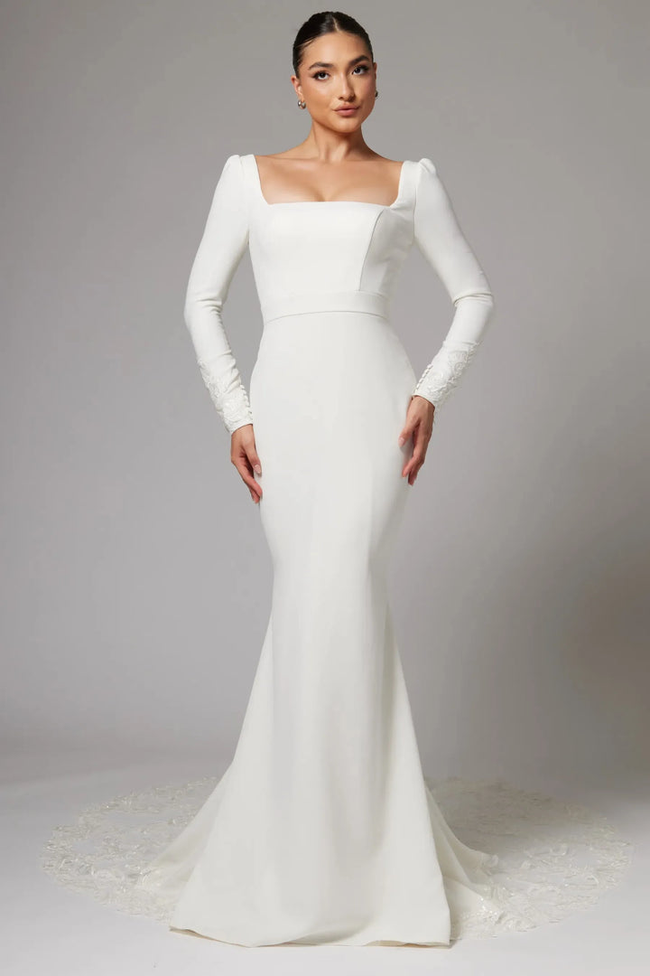 Woman wearing a white wedding dress with long sleeves on a plain background