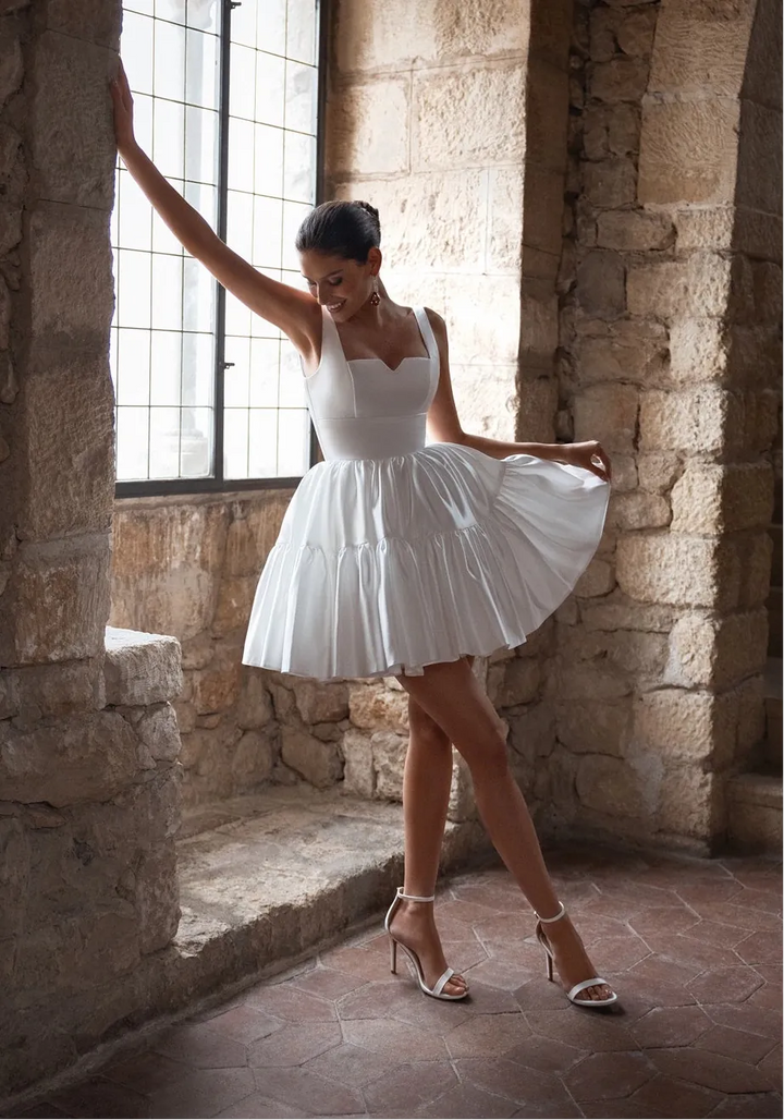 Woman in a white dress standing in a stone-walled room with large windows.