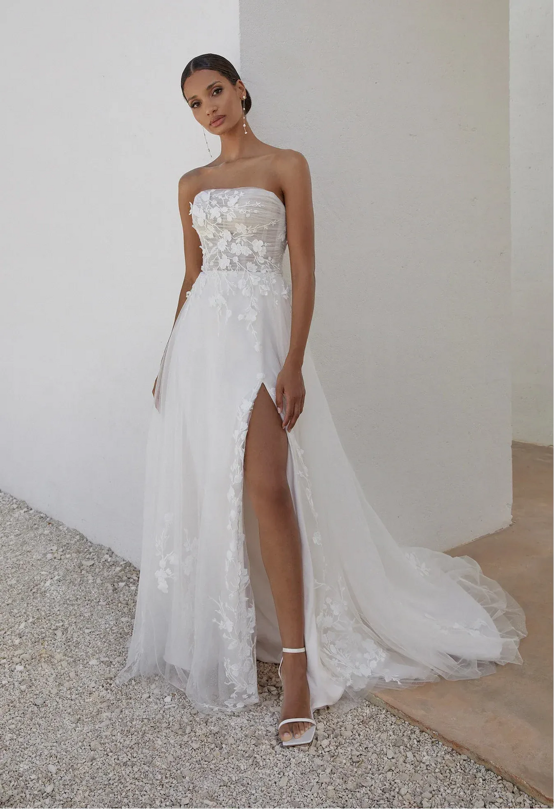 Woman wearing a strapless white wedding dress with a high slit on a neutral background