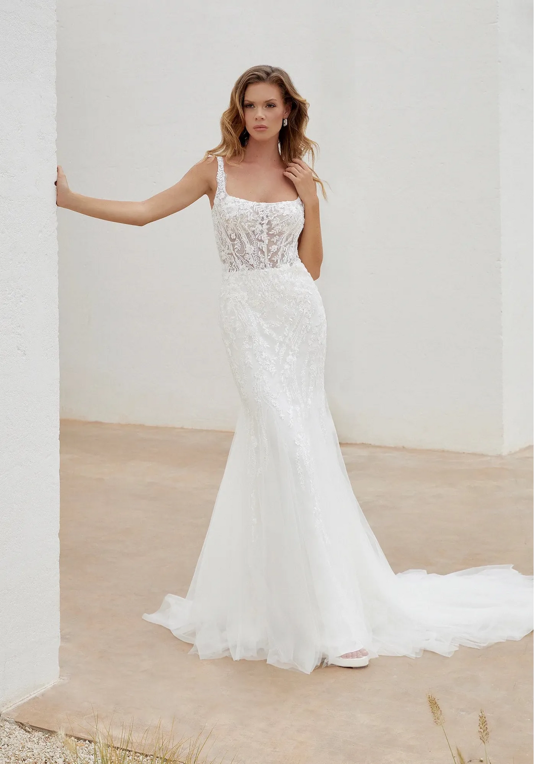 Woman wearing a white lace wedding dress against a plain background