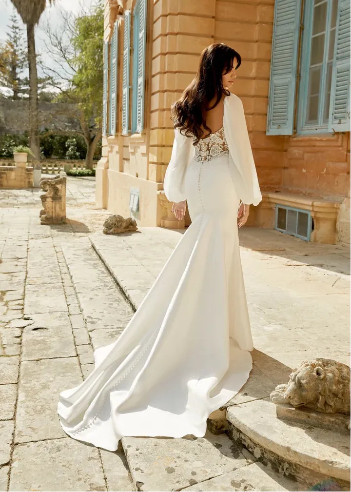 Woman in a white dress standing in front of a stone building with blue shutters.