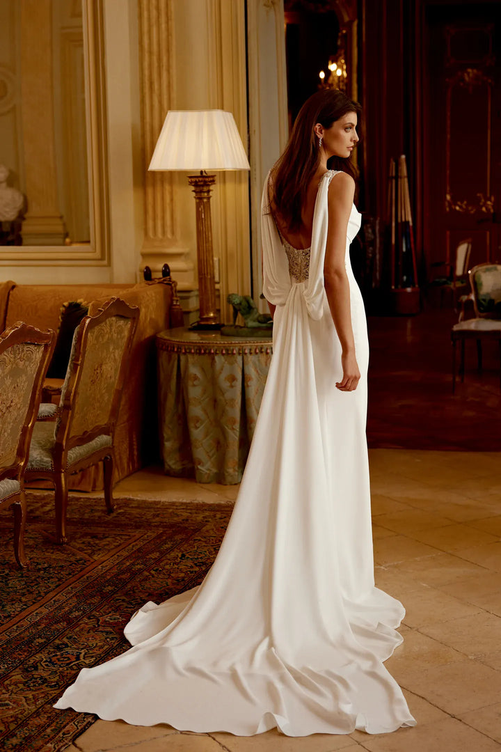 Woman in a white wedding dress standing in an elegant room with wooden furniture and a lamp.