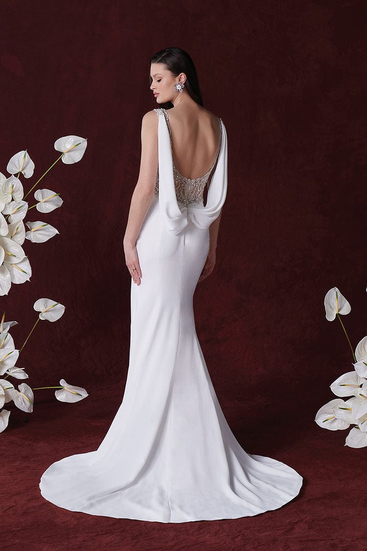Woman in a white wedding dress with a deep neckline, standing against a dark red background with white flowers.