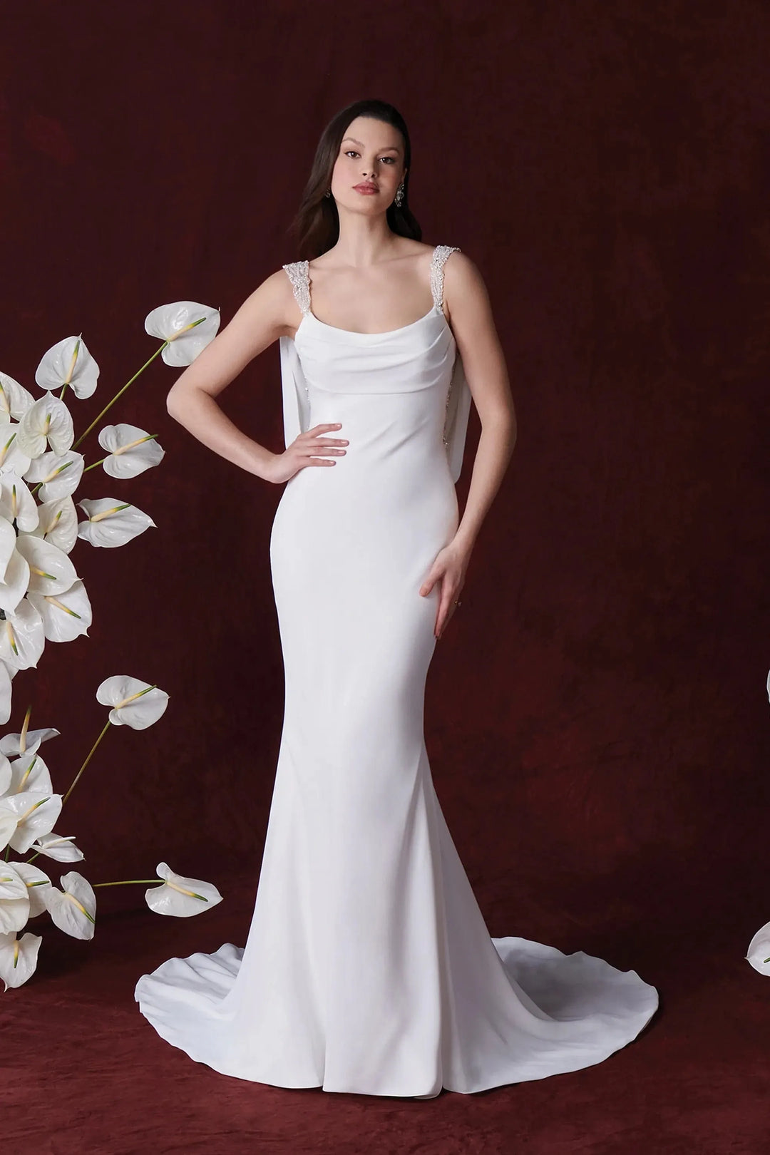 Woman in a white wedding dress standing against a dark background with floral decorations.