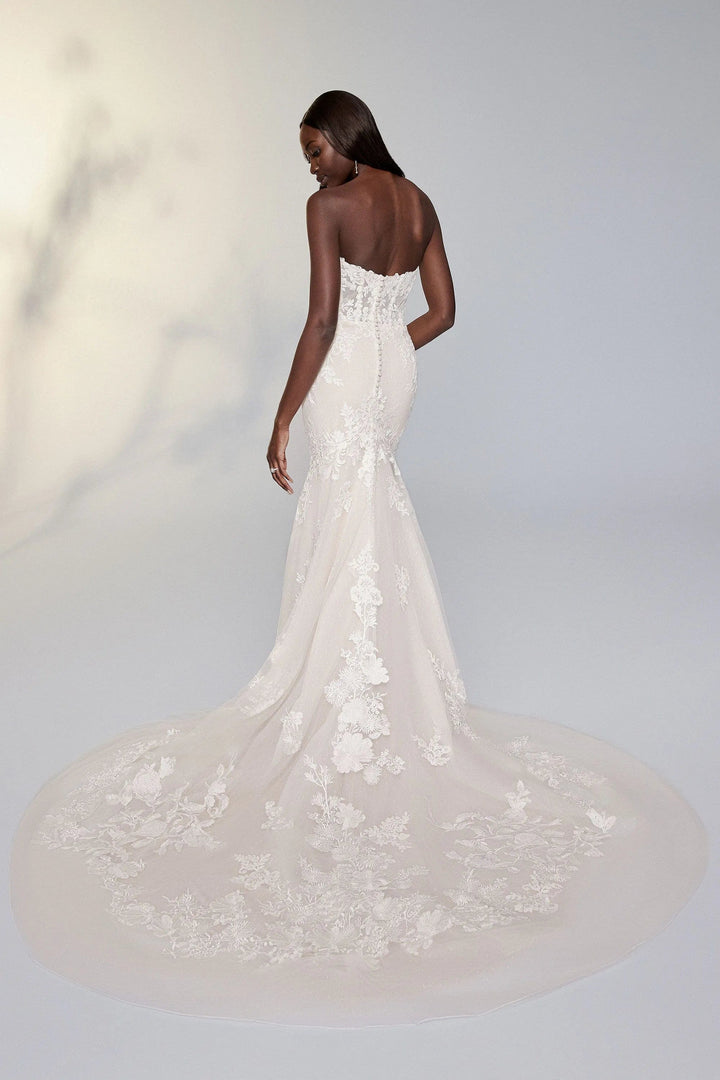 Woman wearing a white wedding dress with a long train on a plain background