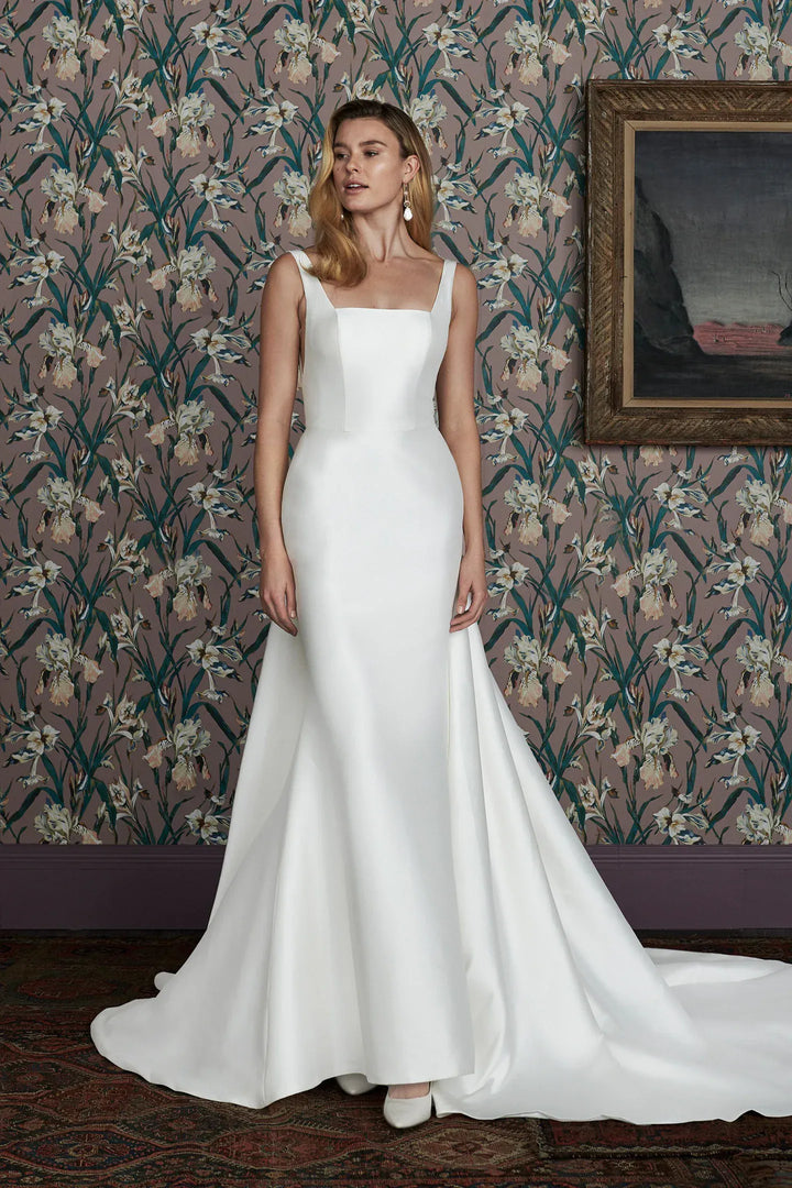 Woman in a white wedding dress standing in a room with floral wallpaper.