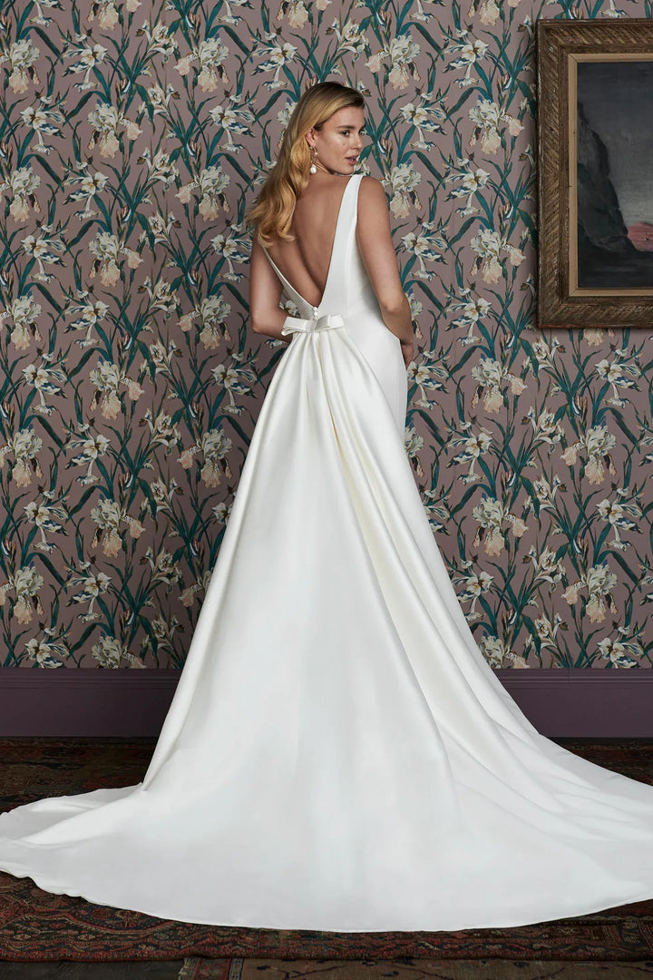 Woman in a white wedding dress with a long train standing in front of floral wallpaper.