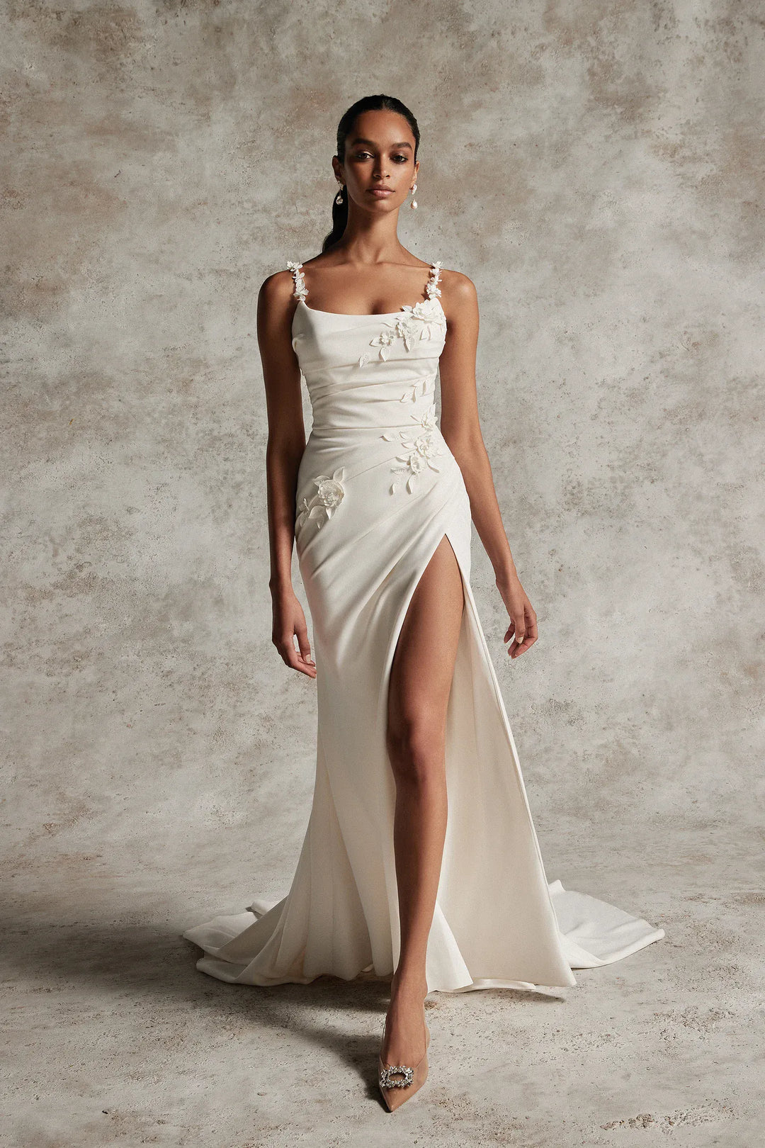 Woman wearing a white wedding dress with a high slit on a textured gray background