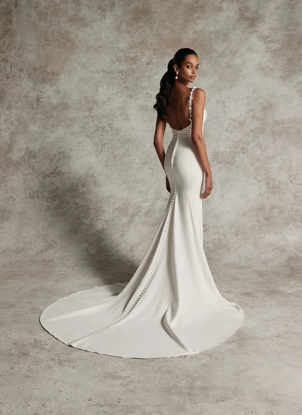 Woman in a white wedding dress with a long train against a textured brown background