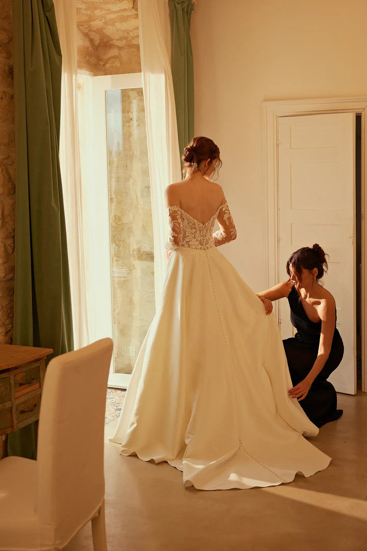Woman trying on a white wedding dress in a room with large windows.