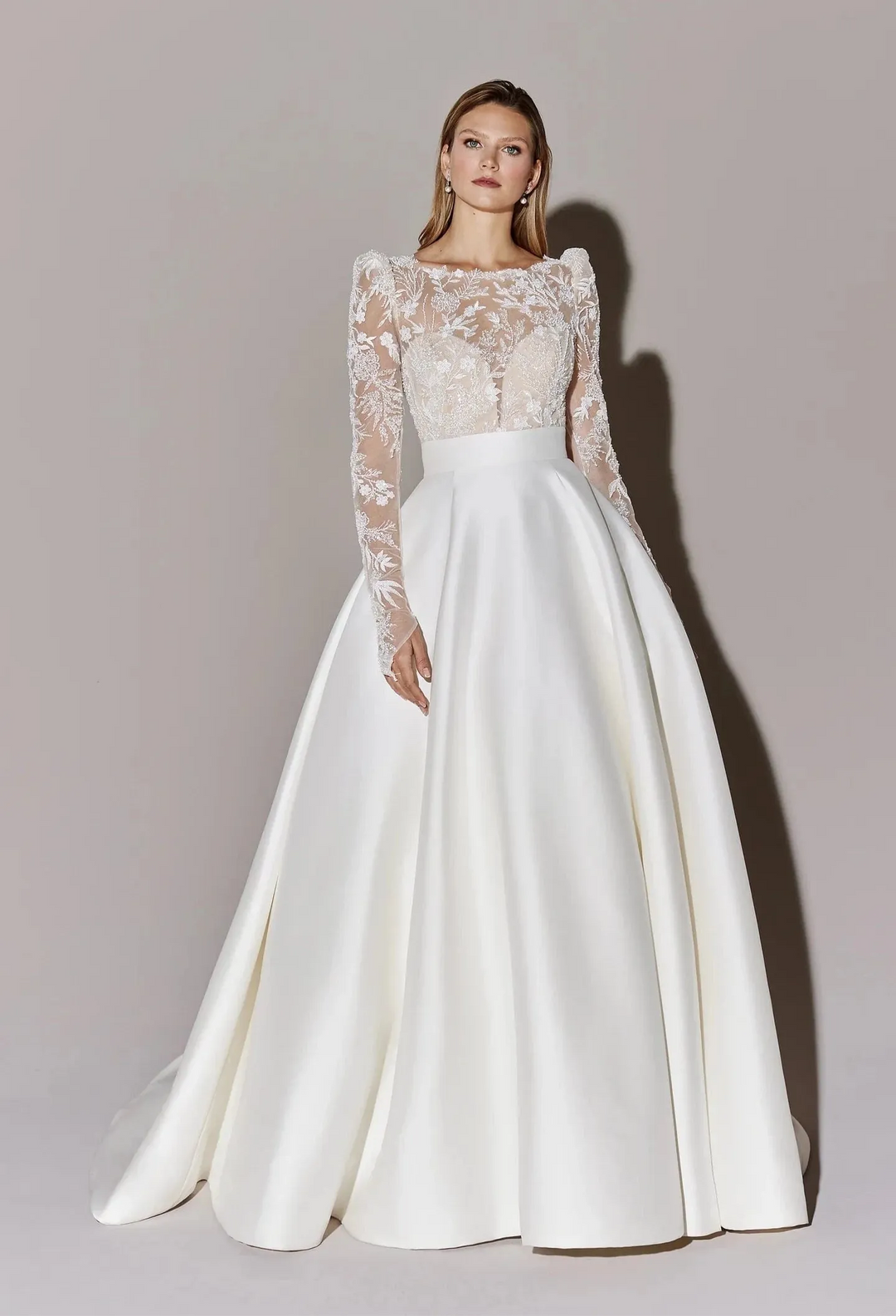 White wedding dress with lace bodice and long sleeves on a plain background