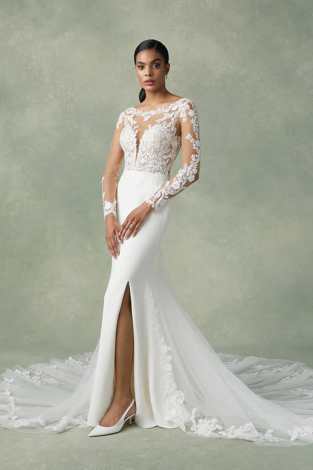 Woman wearing a white lace wedding dress with a high slit on a plain background