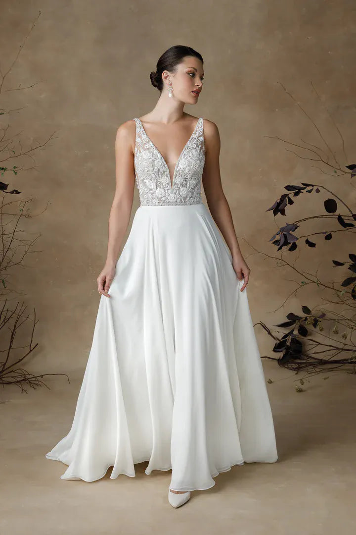 Woman wearing a white wedding dress with lace top and flowing skirt against a neutral background.