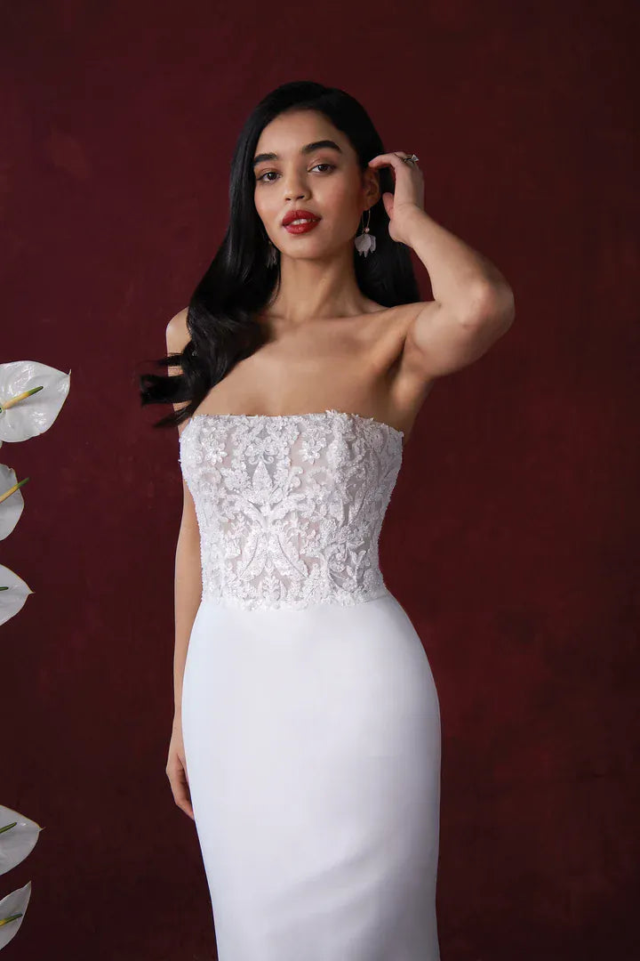Woman wearing a strapless white lace dress against a dark red background