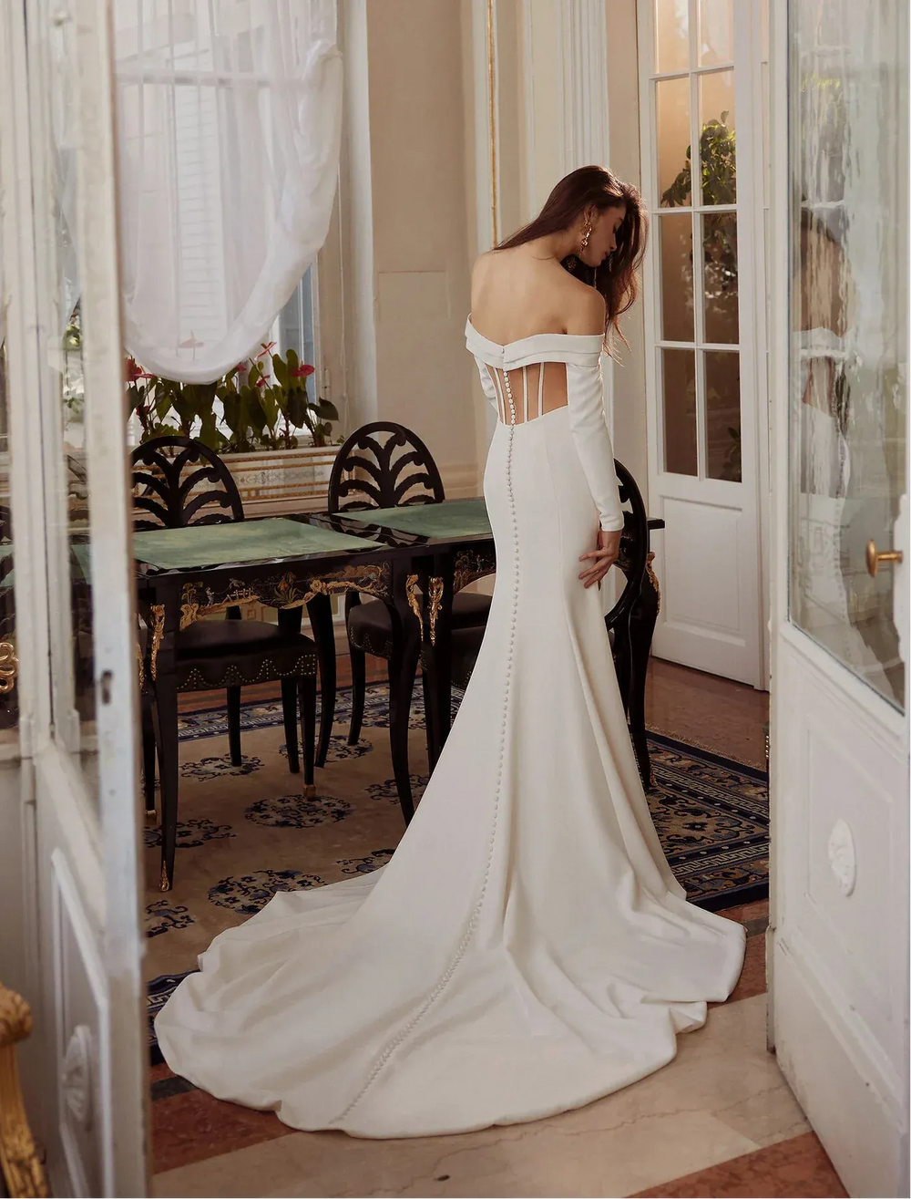 Woman in a white wedding dress standing in a elegant room with a dining table and chairs.