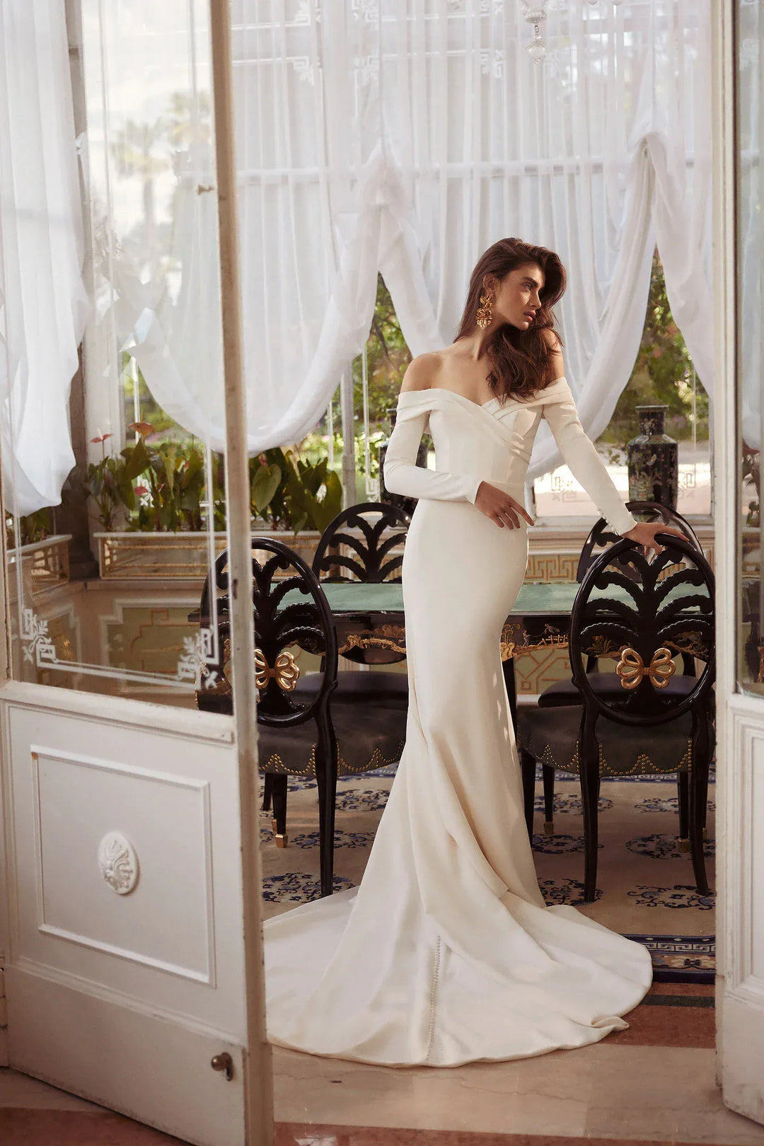 Woman in a white off-shoulder wedding dress standing in a decorated room with curtains.