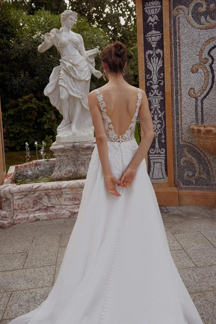Woman in a white wedding dress standing in front of a classical statue and mosaic wall.