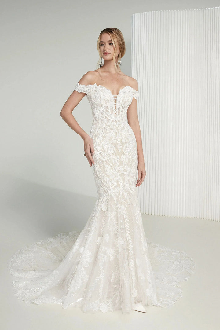 Woman wearing a white off-shoulder wedding dress with floral details against a plain background