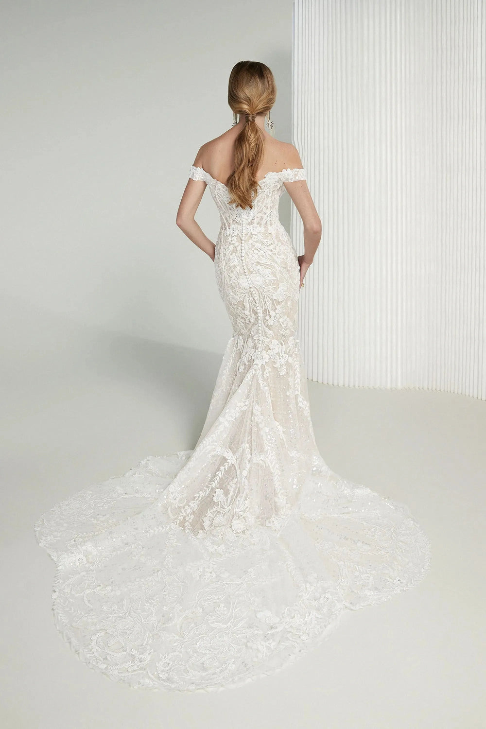 Woman wearing a white lace wedding dress against a plain background