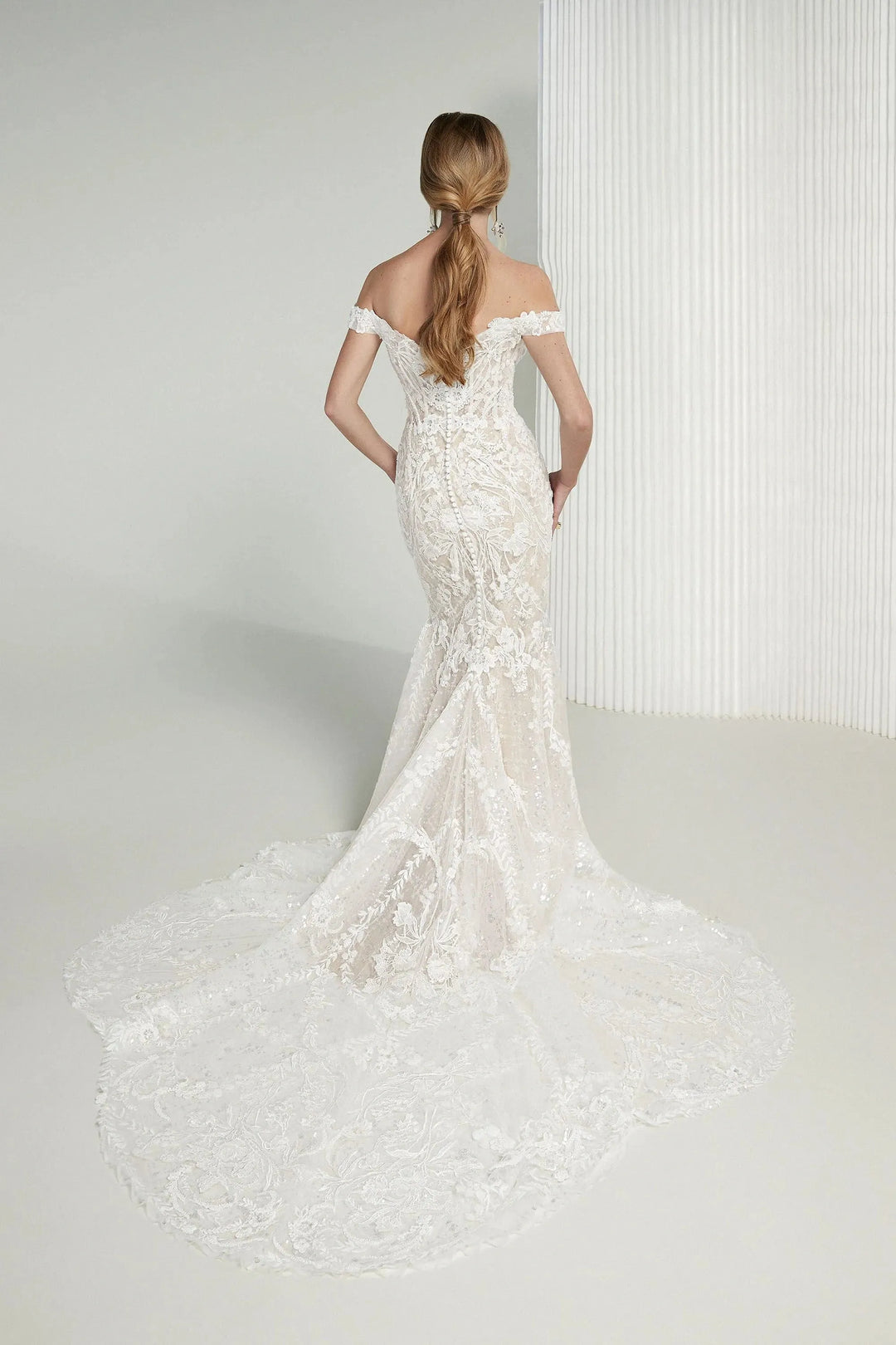 Woman wearing a white lace wedding dress against a plain background