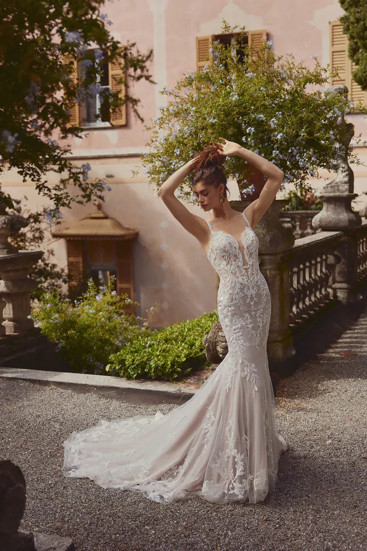 Woman in a white lace wedding dress standing outdoors with classical architecture in the background
