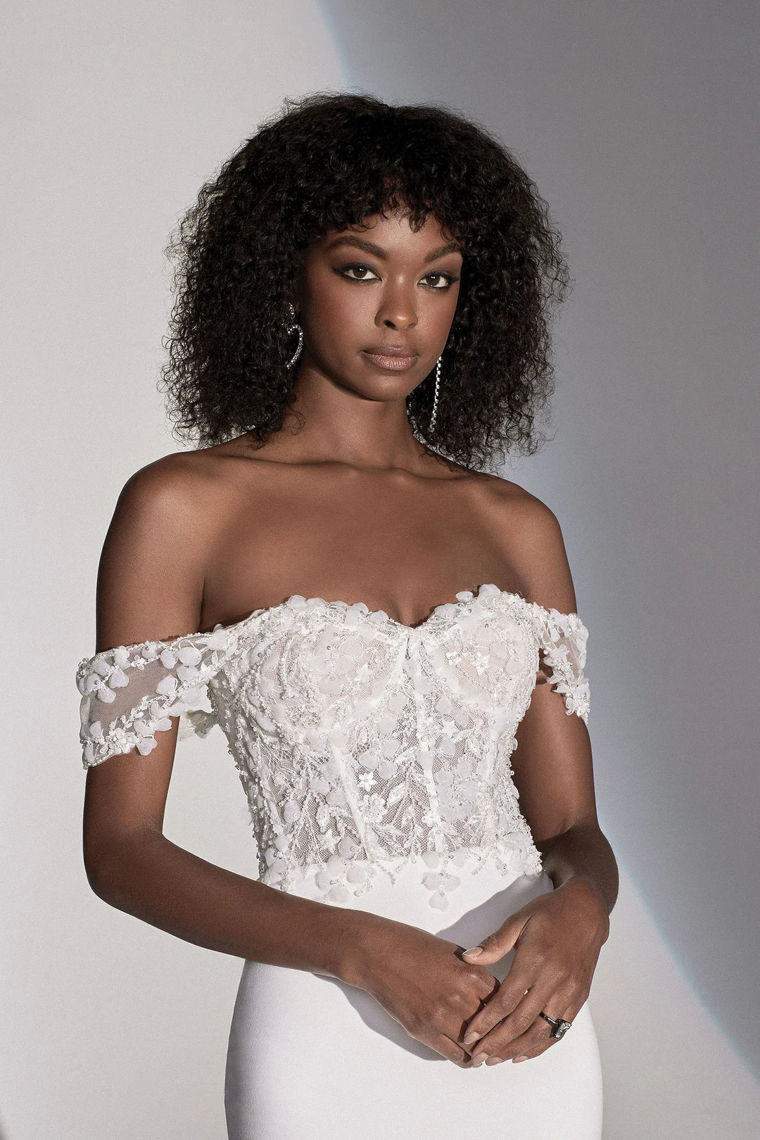 Woman wearing a white off-shoulder lace dress against a plain background