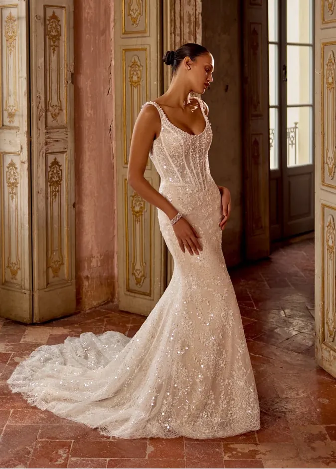 Woman in a white lace wedding dress standing in an ornate room with decorative walls.