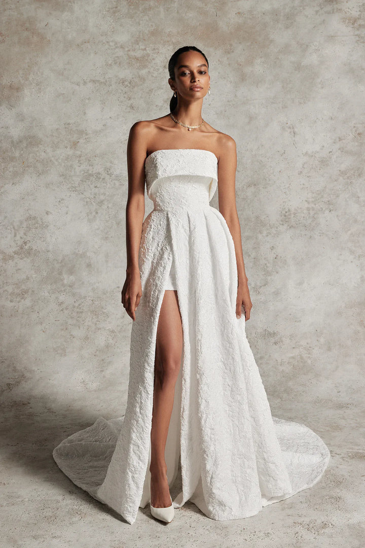 Woman wearing a strapless white wedding dress with a high slit on a textured gray background