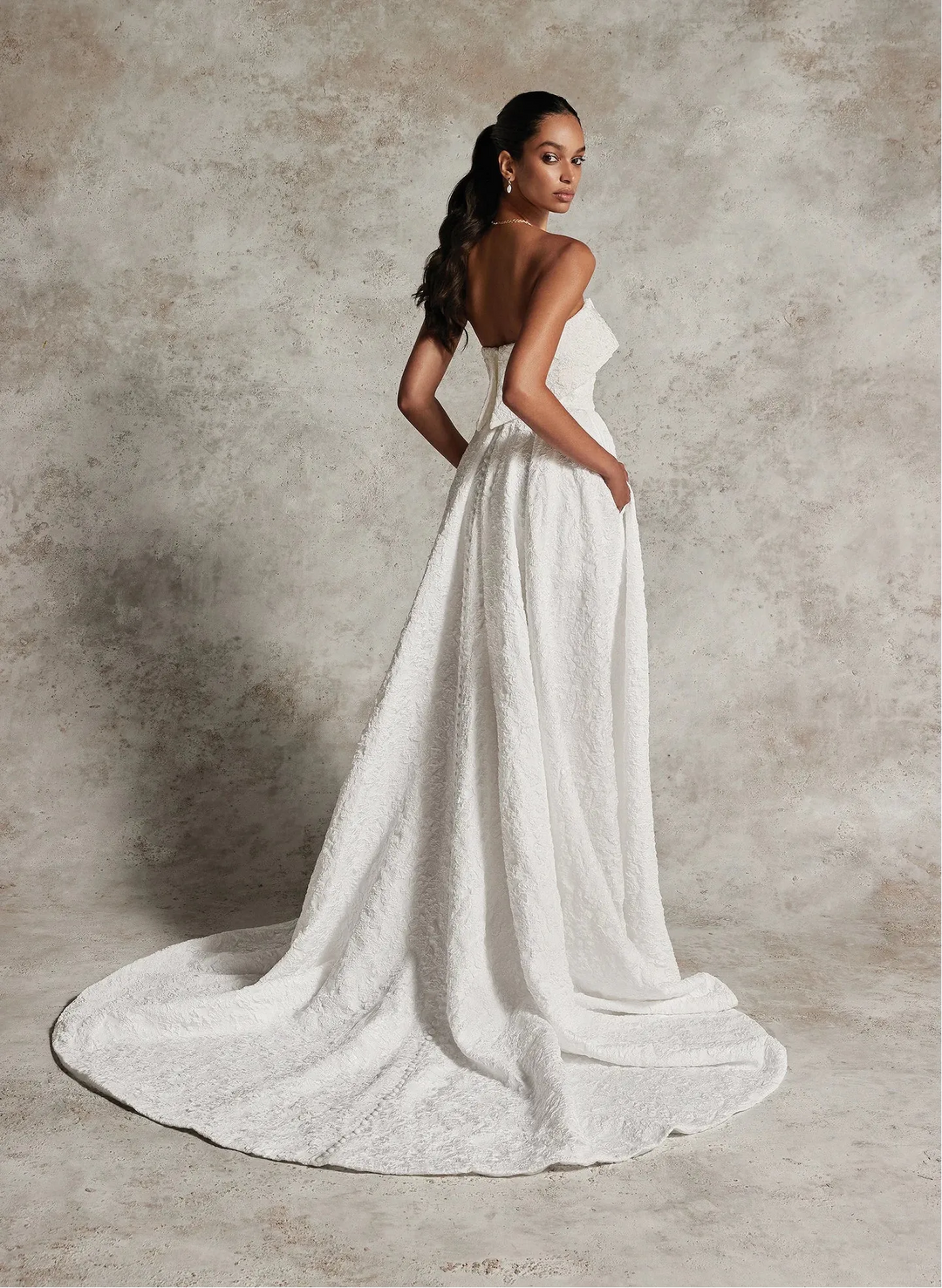 Woman in a white wedding dress standing against a textured gray background