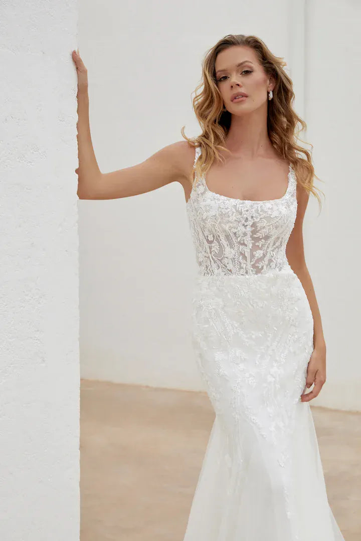 Woman wearing a white lace wedding dress against a plain background