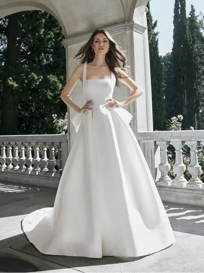 Woman in a white wedding dress standing on a balcony with trees in the background
