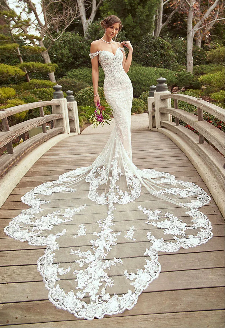 Woman in a white wedding dress with a long train standing on a wooden bridge in a garden setting.