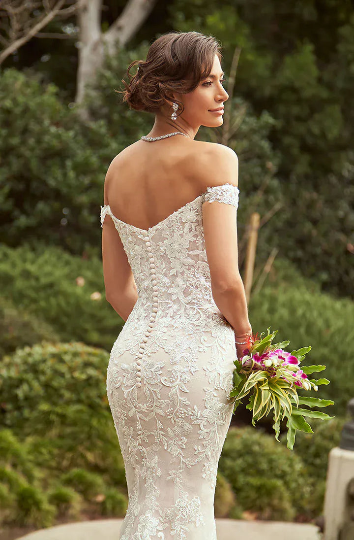 Woman in a white lace wedding dress holding a bouquet outdoors.
