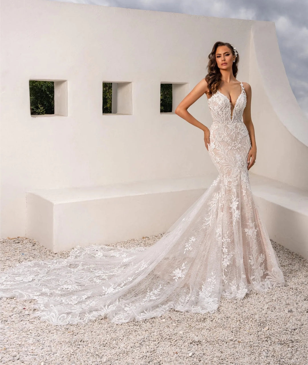 Woman in a white wedding dress standing in front of a modern architectural structure with a cloudy sky.