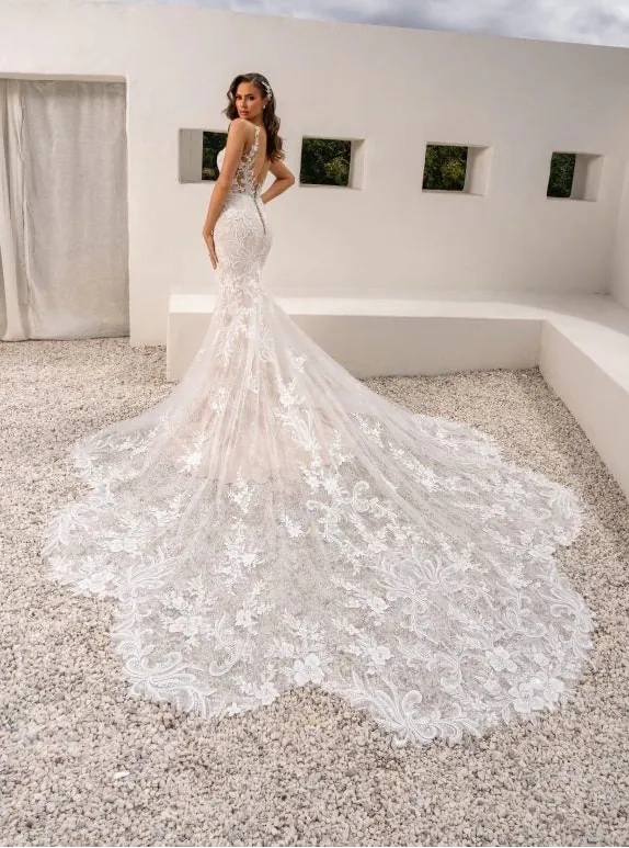 Woman in a white wedding dress standing in a modern outdoor setting with a cloudy sky.