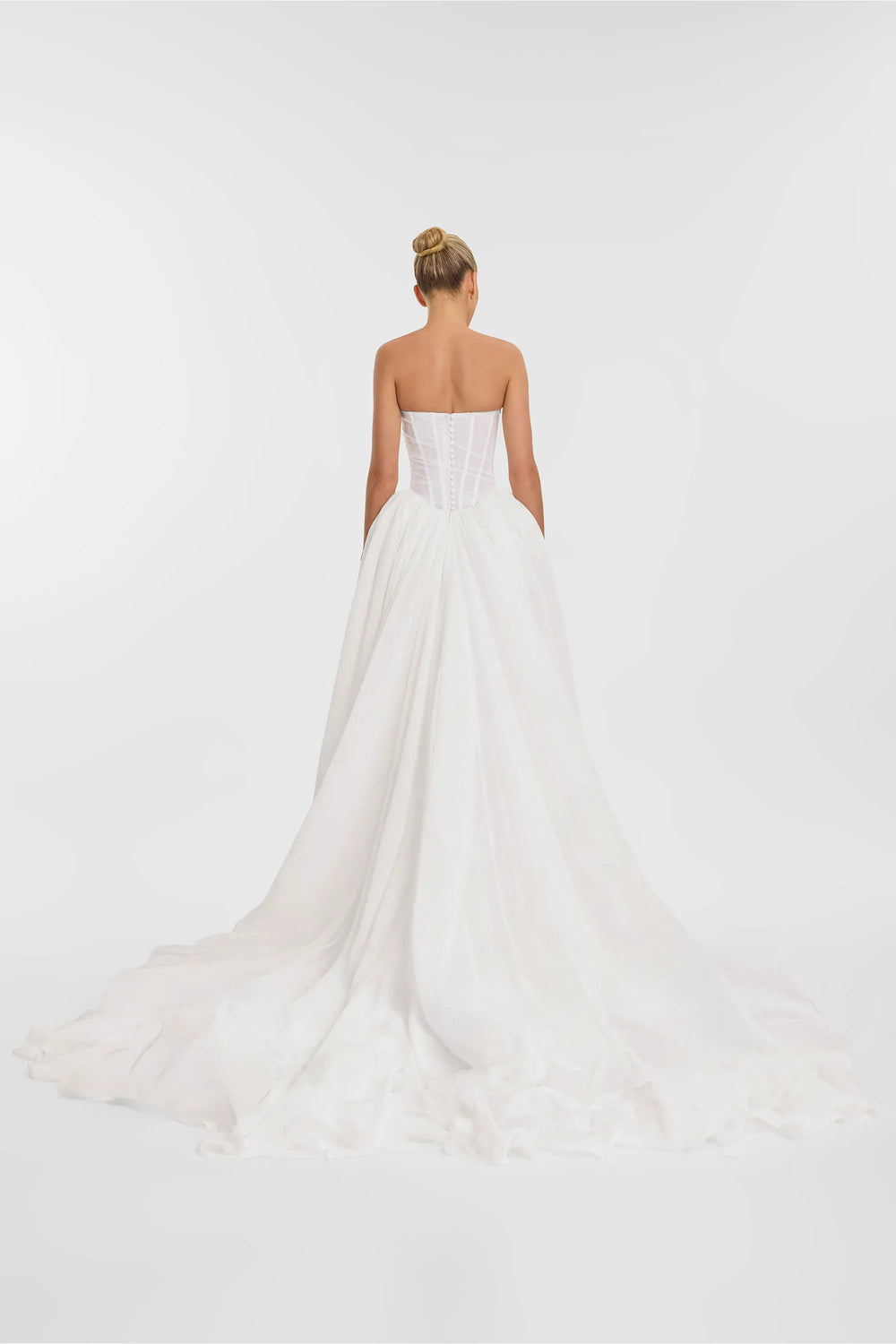 Woman wearing a strapless white wedding dress on a plain background