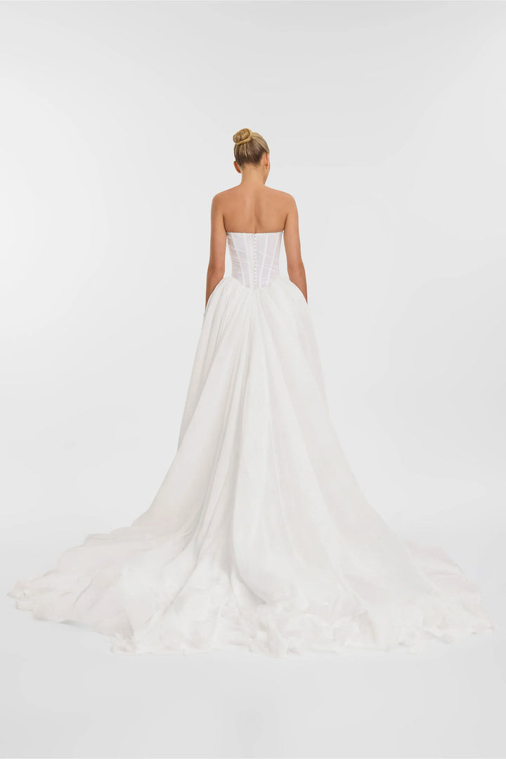 Woman wearing a strapless white wedding dress on a plain background