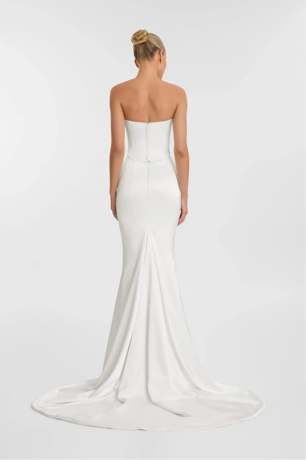 Woman wearing a strapless white wedding dress on a plain background