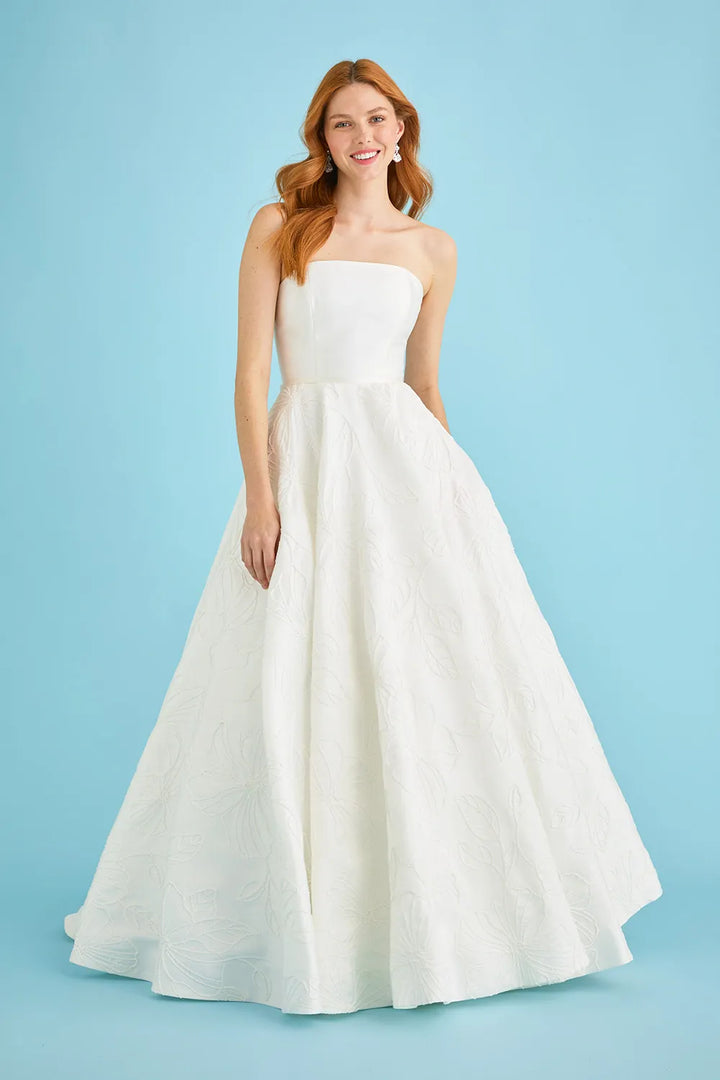 A woman modeling a strapless white ball gown with a structured bodice and a full, flowing skirt against a solid light blue studio background.