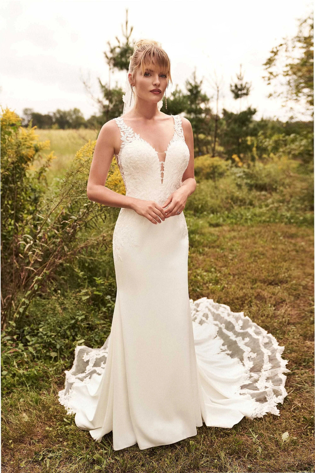 Woman in a white wedding dress standing in a natural setting with greenery.