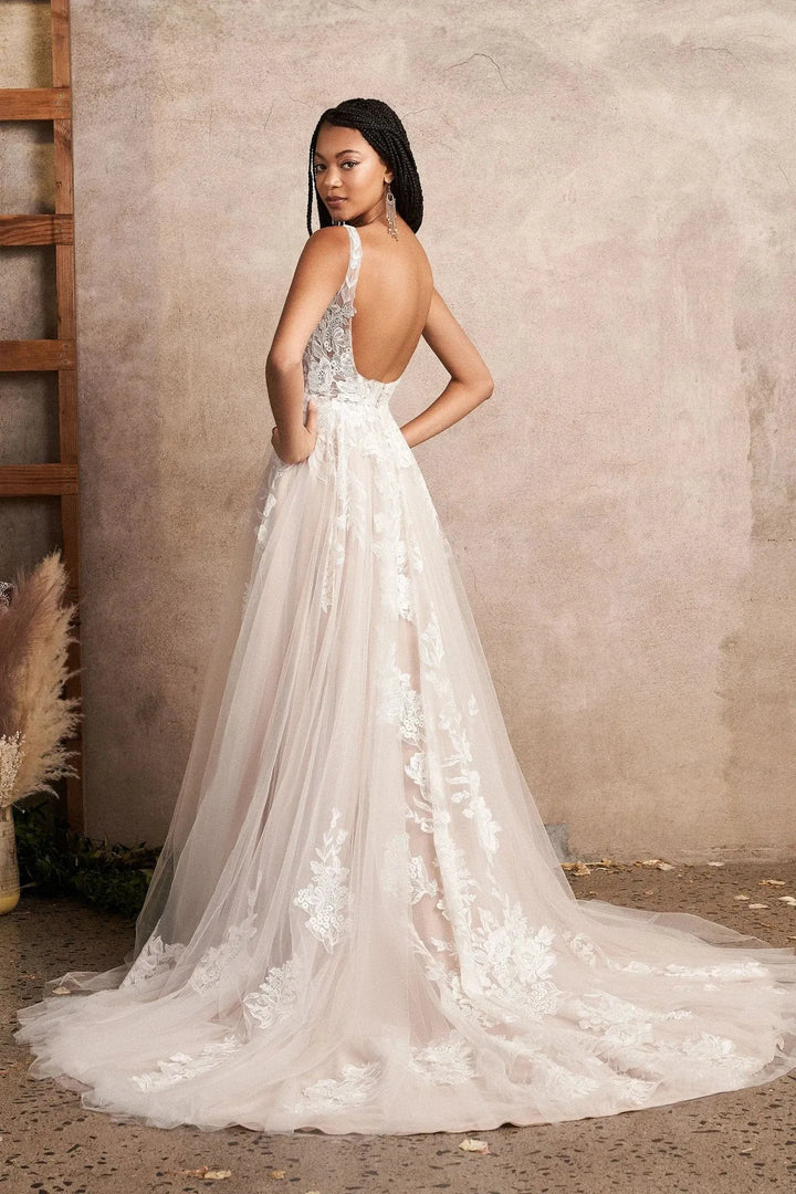 Woman wearing a white lace wedding dress with an open back against a neutral wall.