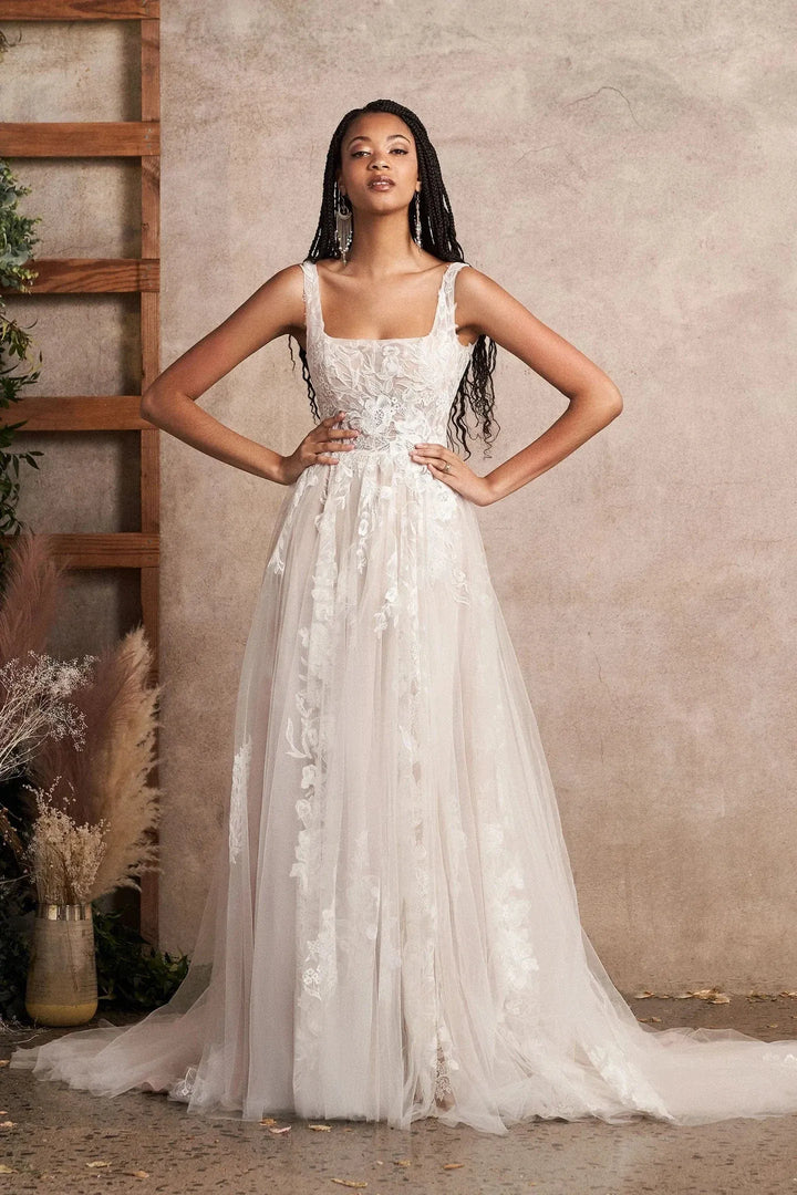 Woman in a white floral wedding dress standing against a neutral wall.