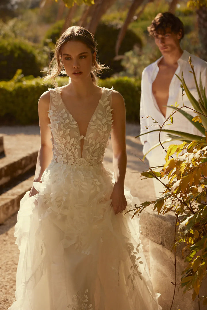 Woman in a white wedding dress standing outdoors with a man in the background.
