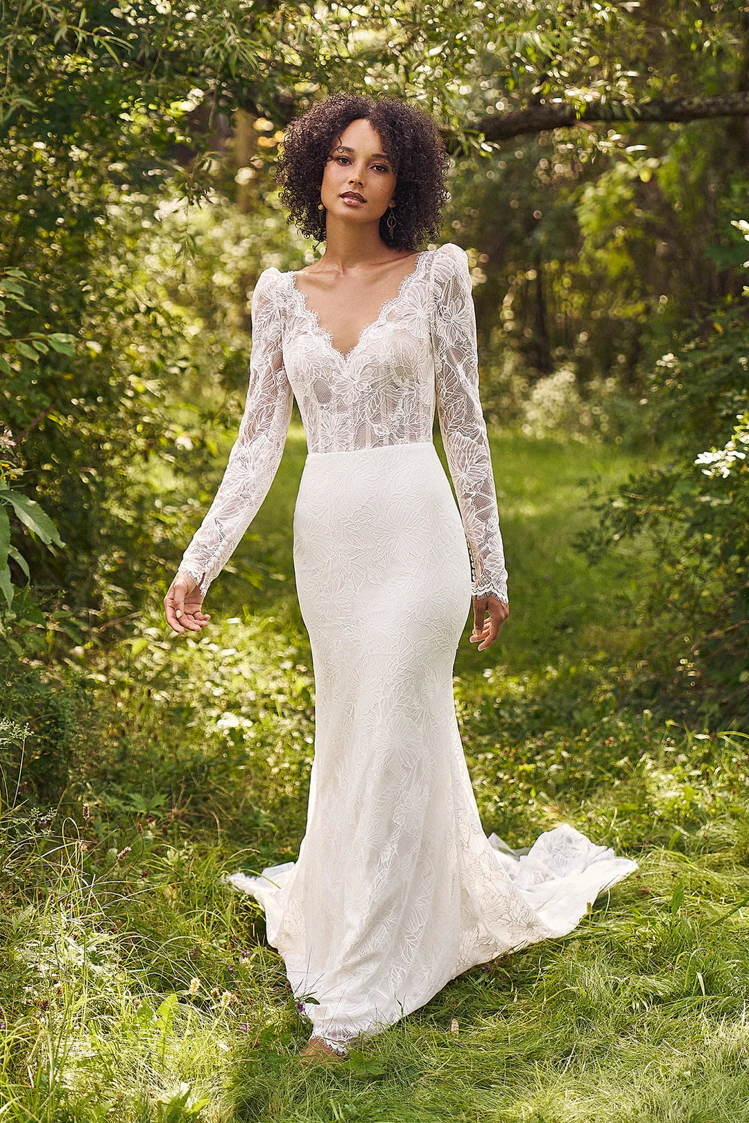 Woman in a white lace wedding dress standing in a forest