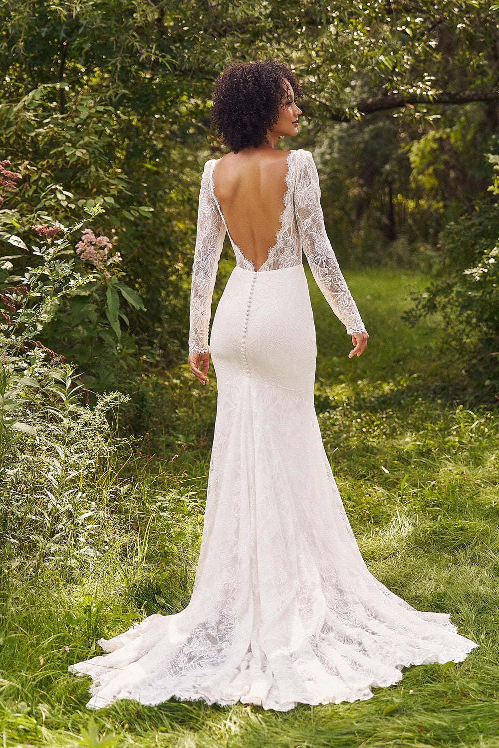 Woman in a white lace wedding dress standing in a natural setting with greenery.