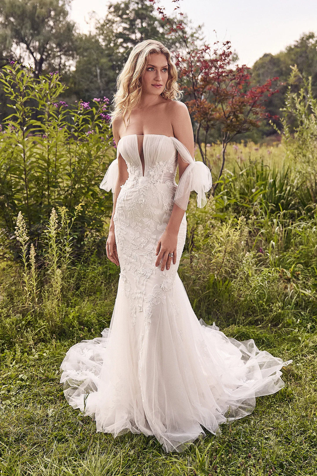 Woman in a white wedding dress standing in a natural setting with greenery.