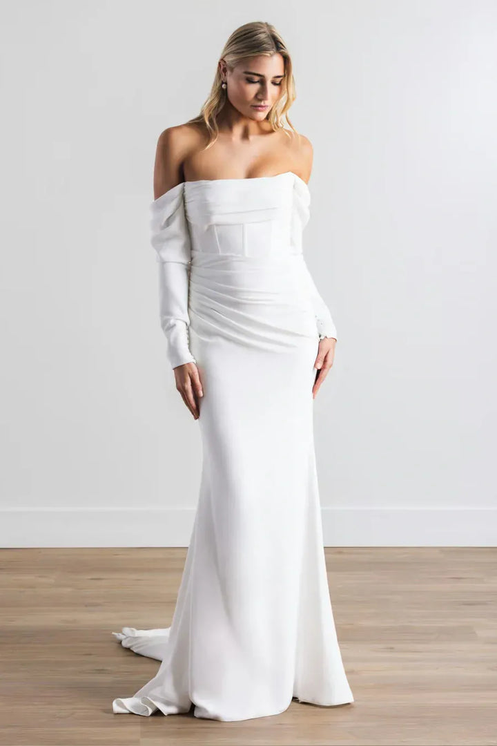 Woman wearing a white off-shoulder gown against a plain background