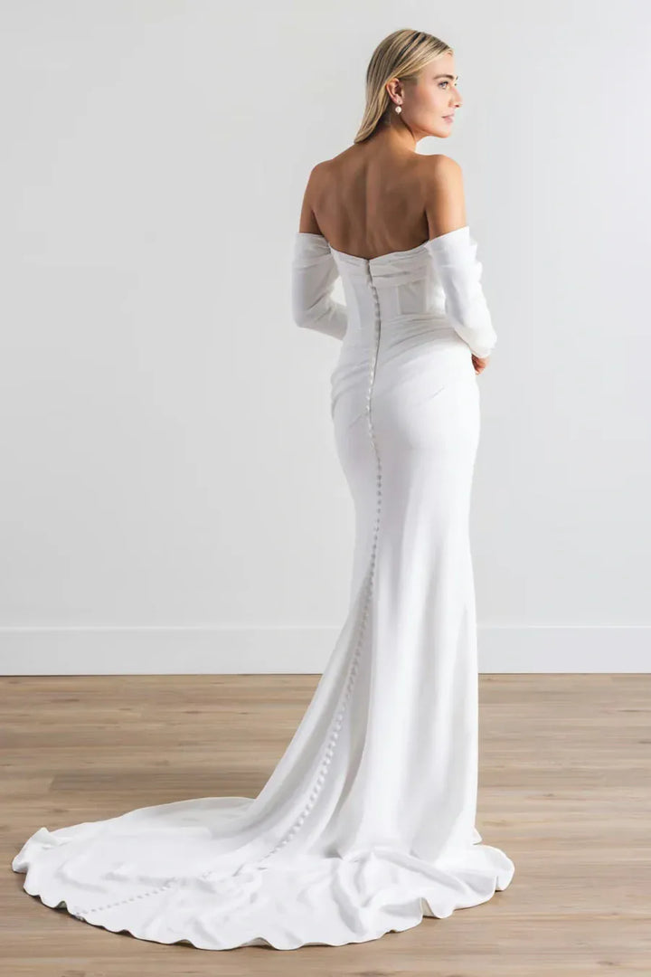 Woman wearing a white off-shoulder gown with a long train on a plain background